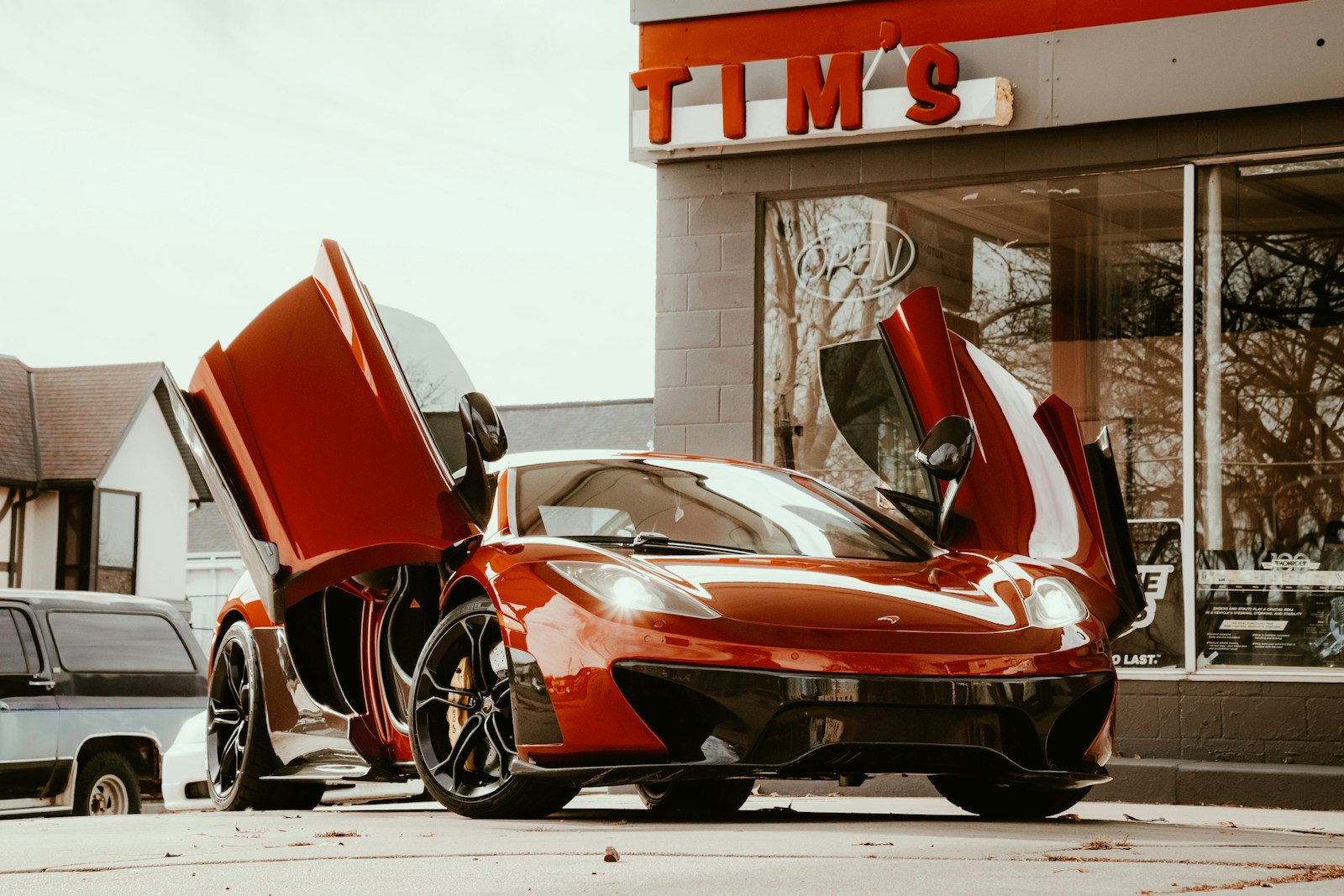 Red exotic sports car with raised doors outside a modern building